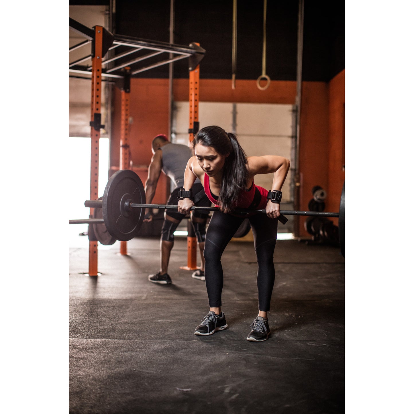 Person lifts barbell in gym, concentrating amid workout equipment.