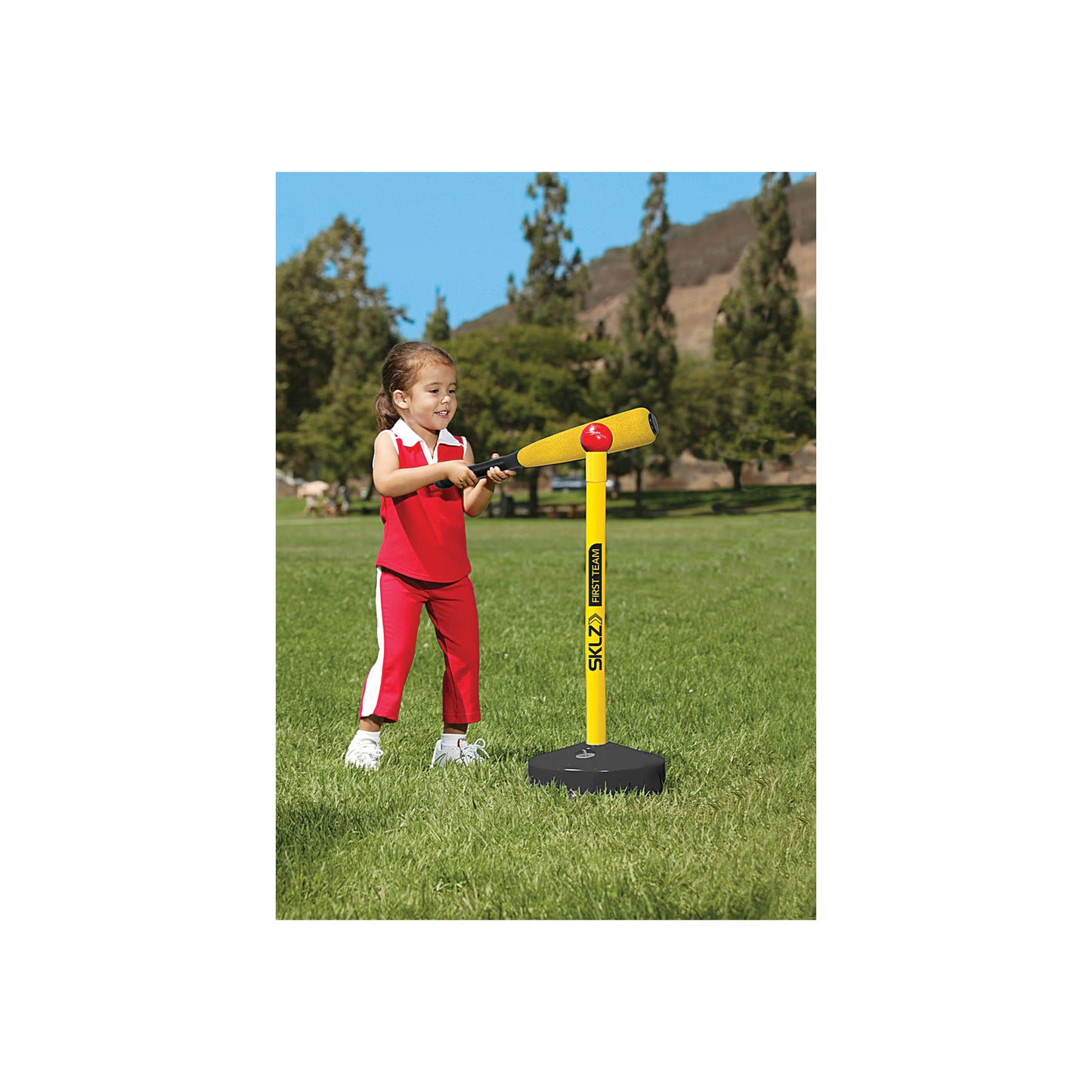 Child hits a ball with a bat on a grassy field in a park