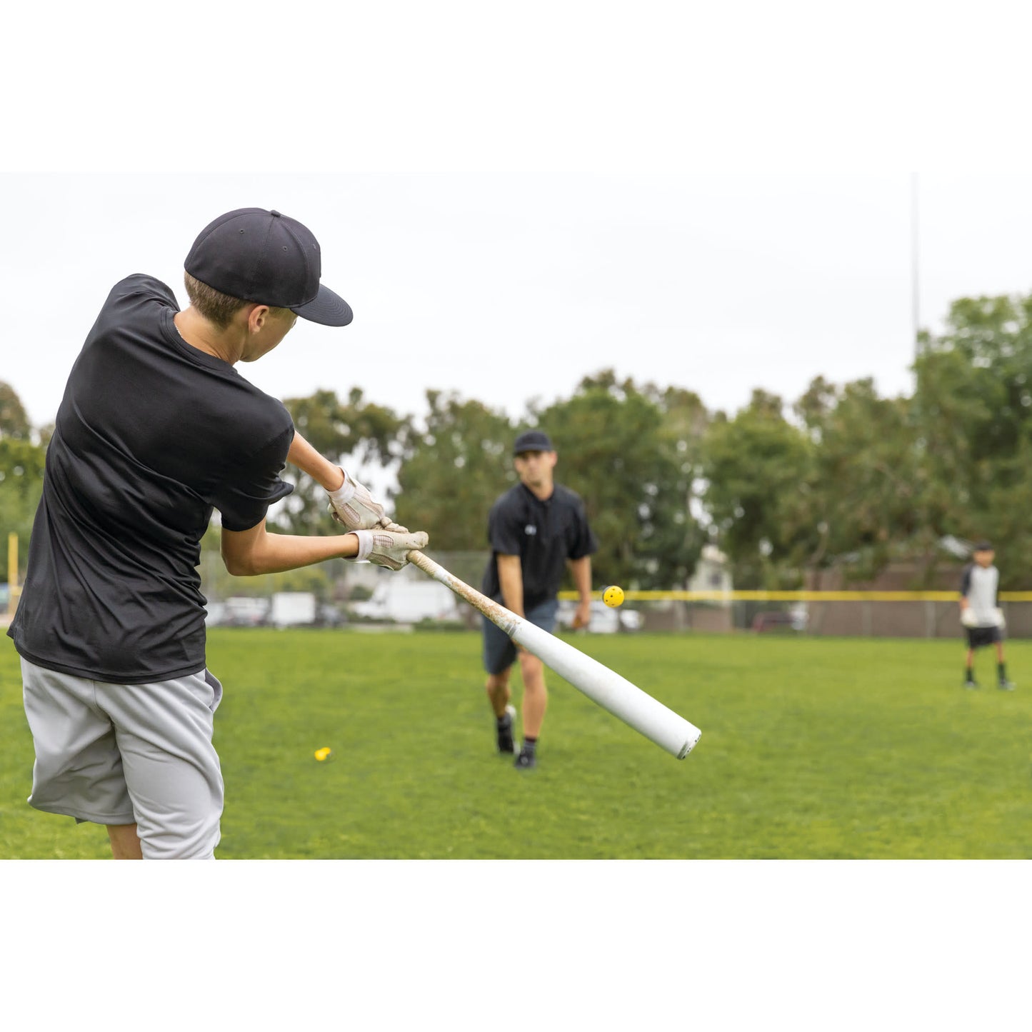 Child swings a baseball bat at a ball on a field during a game practice