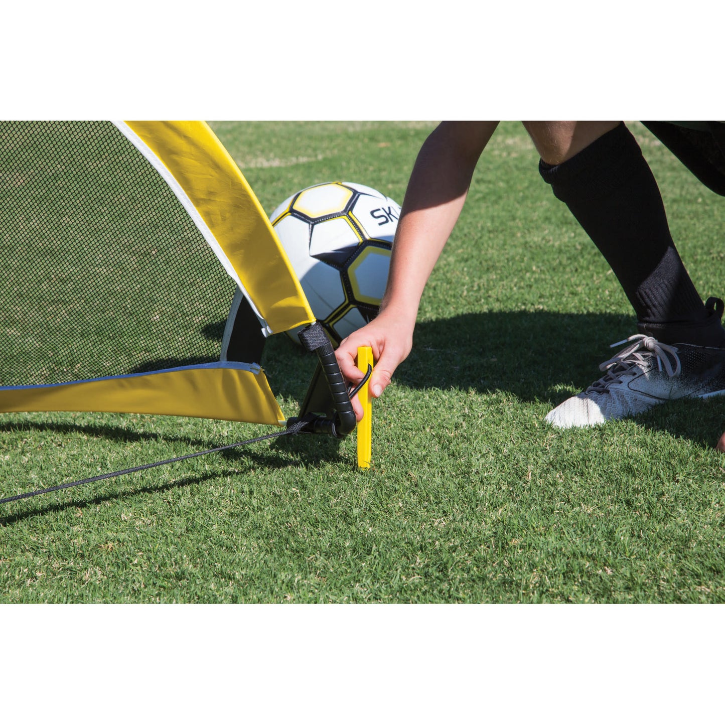 A person sets up a soccer goal on grass with a soccer ball nearby