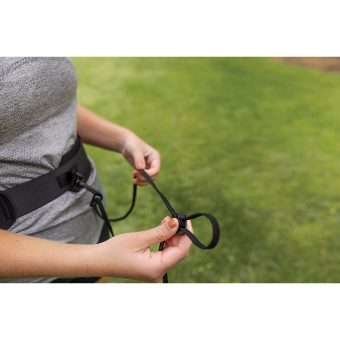 Person secures a leash on a harness outdoors on green grass