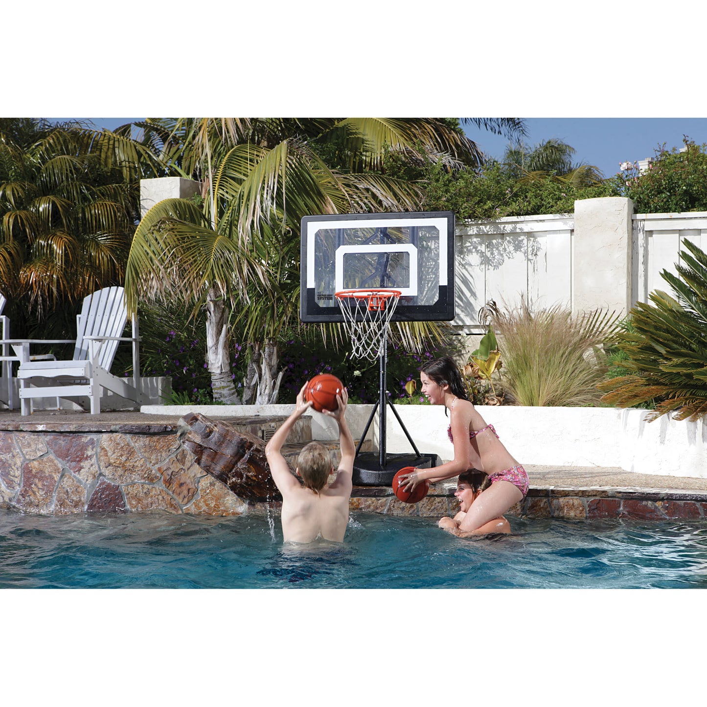 Children playing basketball in a backyard pool with a net and lush tropical surroundings
