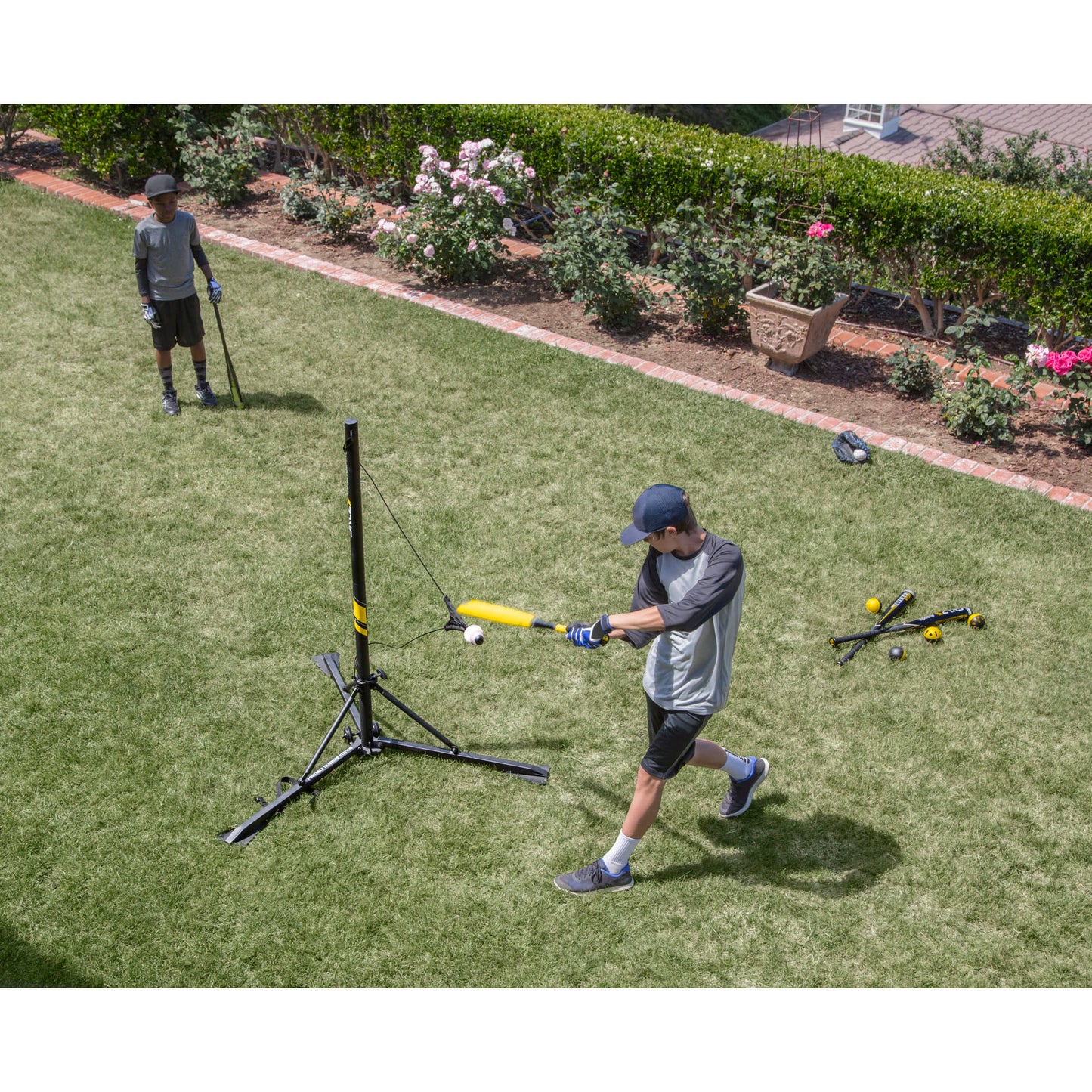 Boy throws baseball at a tee in a garden yard during daytime.