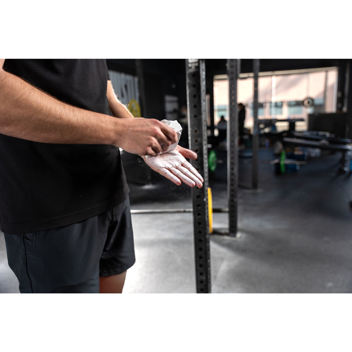 Hands applying chalk in a gym, surrounded by racks and weights.