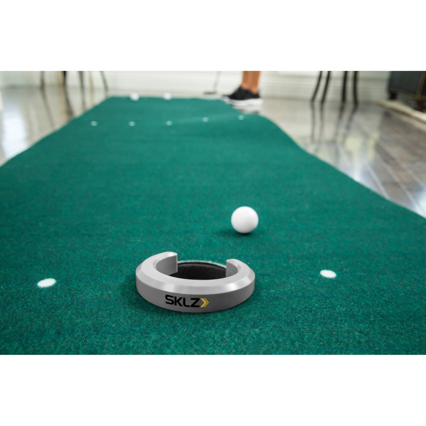The SKLZ data tracker lies on a golf putting green with a golf ball nearby in an indoor environment