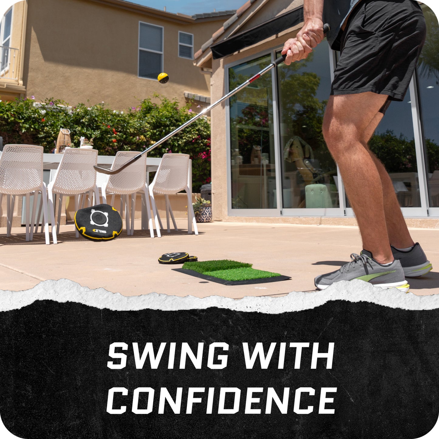 Person practices golf swing on patio with outdoor furniture and greenery in background