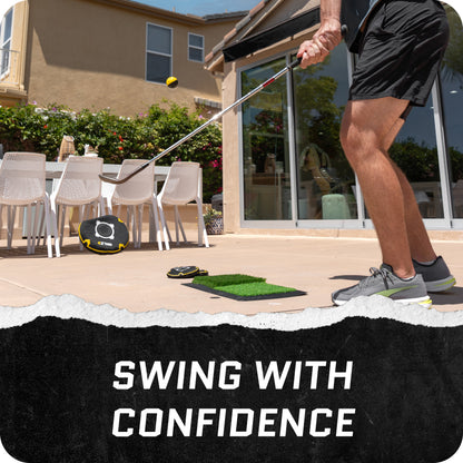 Person practices golf swing on patio with outdoor furniture and greenery in background