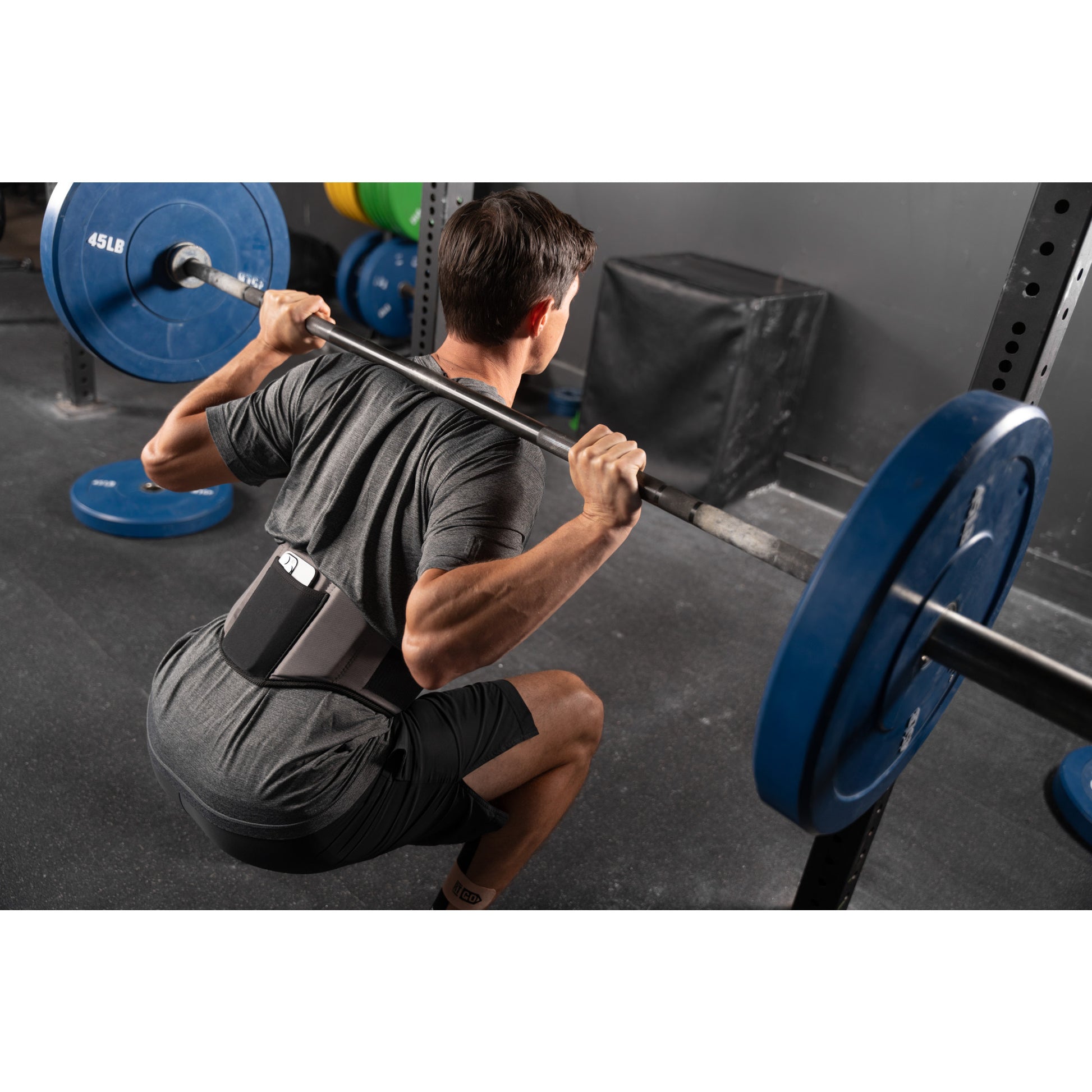 Person squatting with barbell in a gym, wearing a back support belt.
