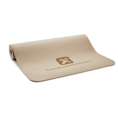 A beige workout mat unrolled on a surface with the Tiggerpoint logo printed on it.
