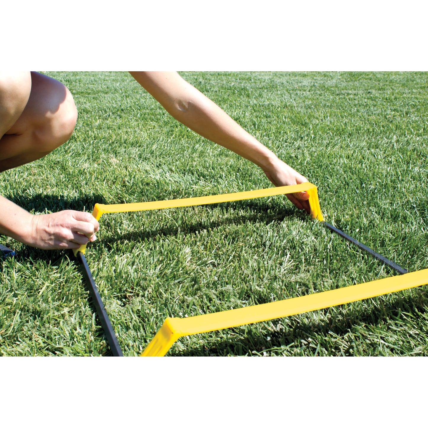 Person adjusts a yellow agility hurdle on a grassy field outdoors