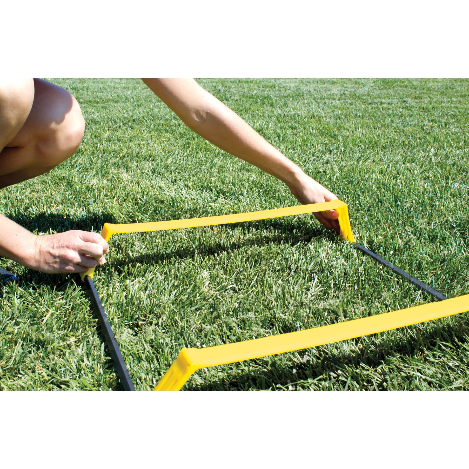 Person adjusts a yellow agility hurdle on a grassy field outdoors