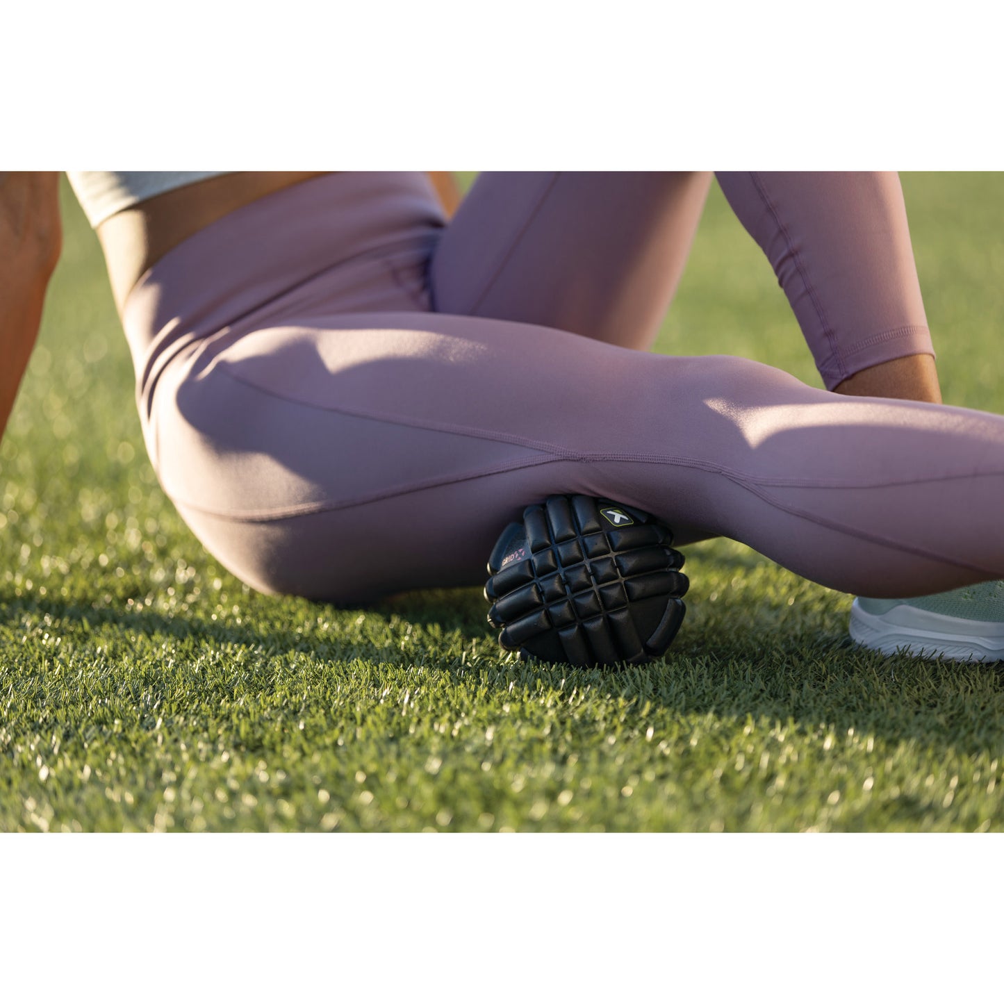 A person uses a massage roller on their thigh outdoors on grass.
