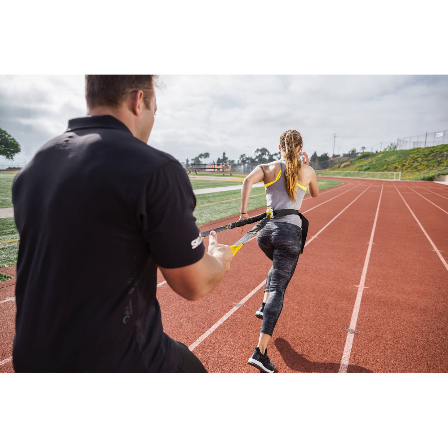 Female athlete using SKLZ Acceleration Trainer with a coach on a track