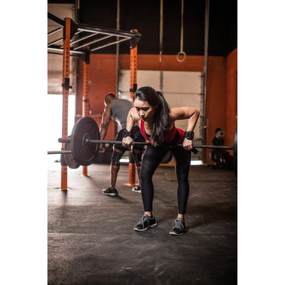 Person lifts barbell in gym, concentrating amid workout equipment.