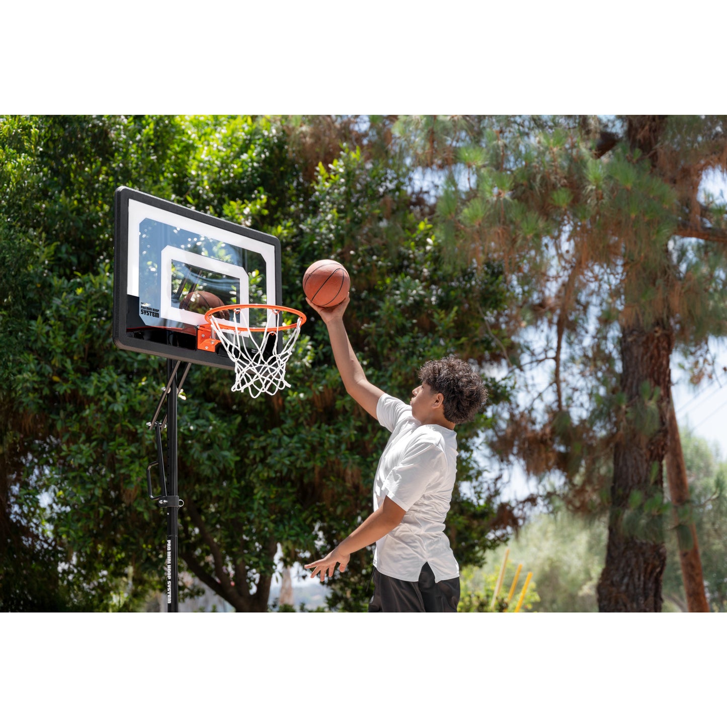 Boy jumps to dunk basketball on outdoor court with trees in the background