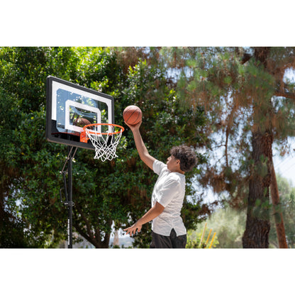 Boy jumps to dunk basketball on outdoor court with trees in the background