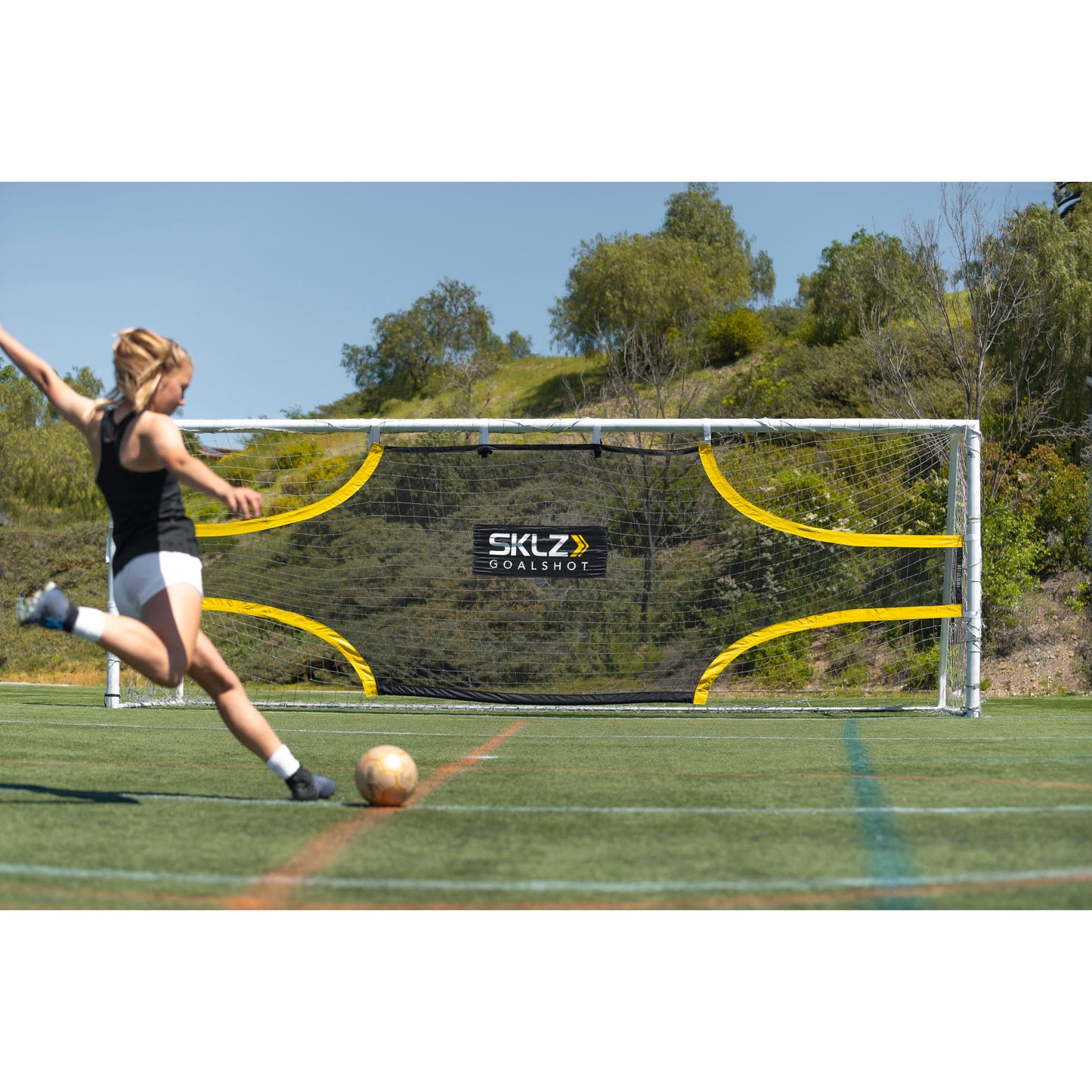 Girl kicks a soccer ball towards a goal on a sunny outdoor field