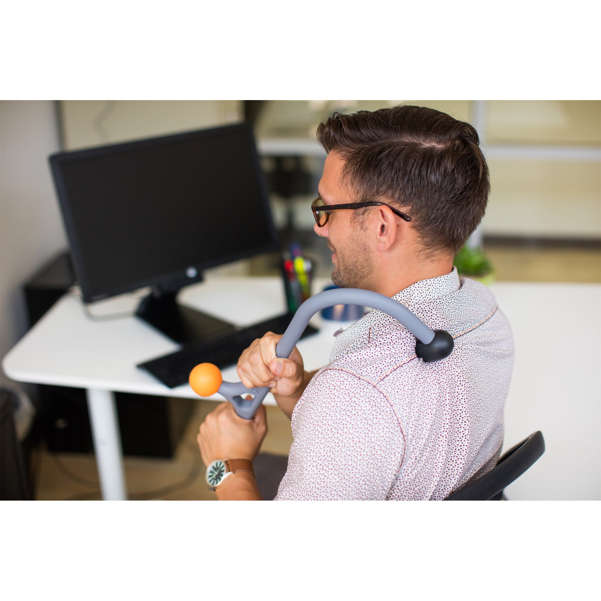 Man sitting at a desk holding a physical therapy device near his shoulder in an office setting