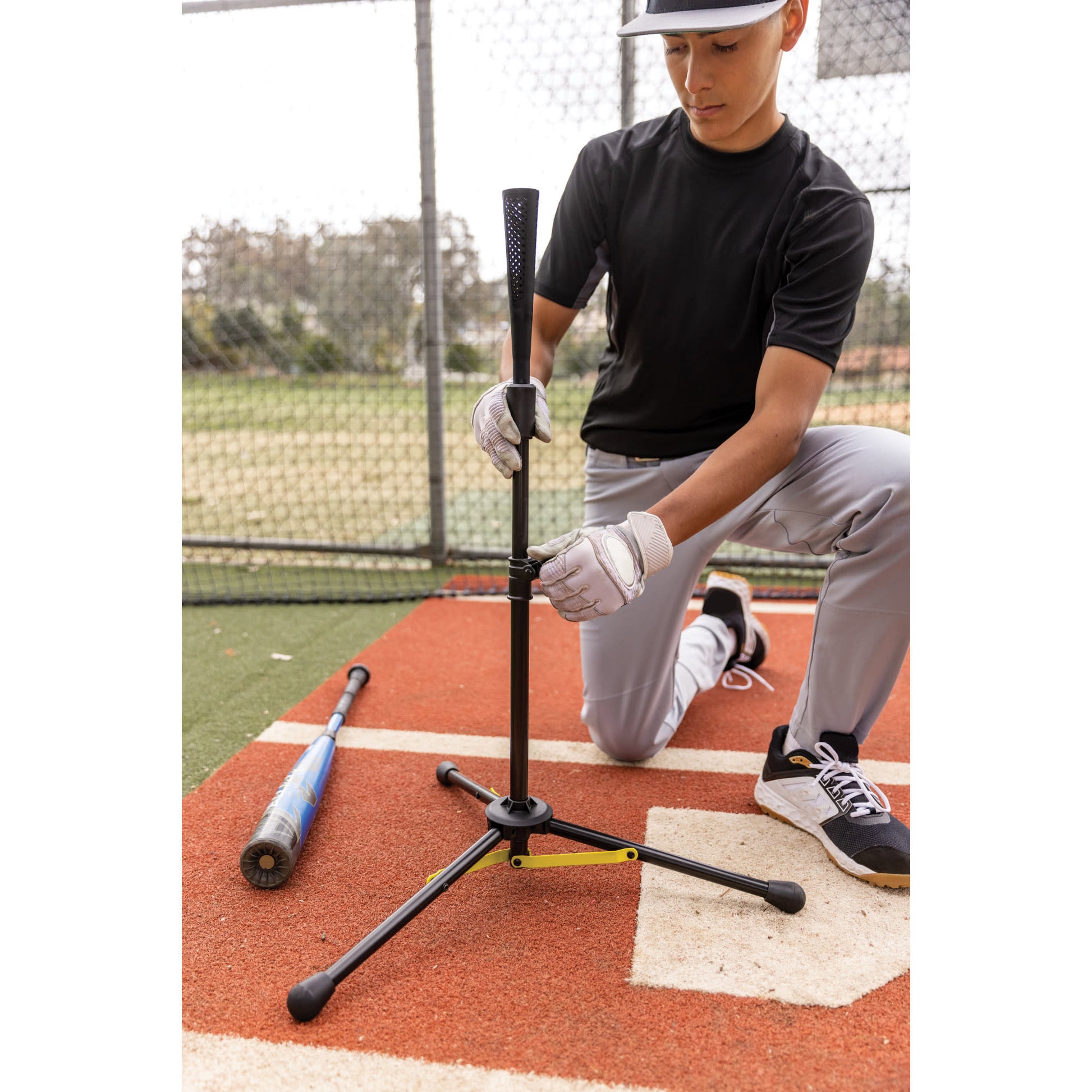 Baseball player adjusts bat stand on field for practice