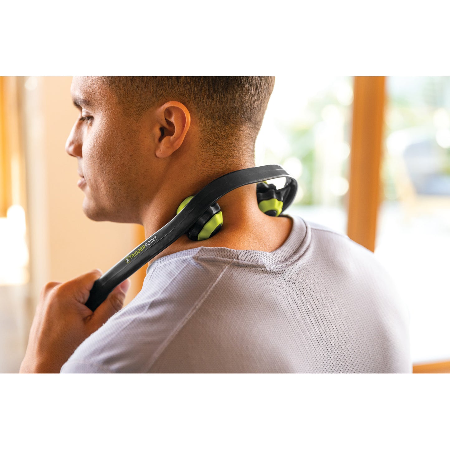 A man massages his neck with a massage device indoors during the daytime.