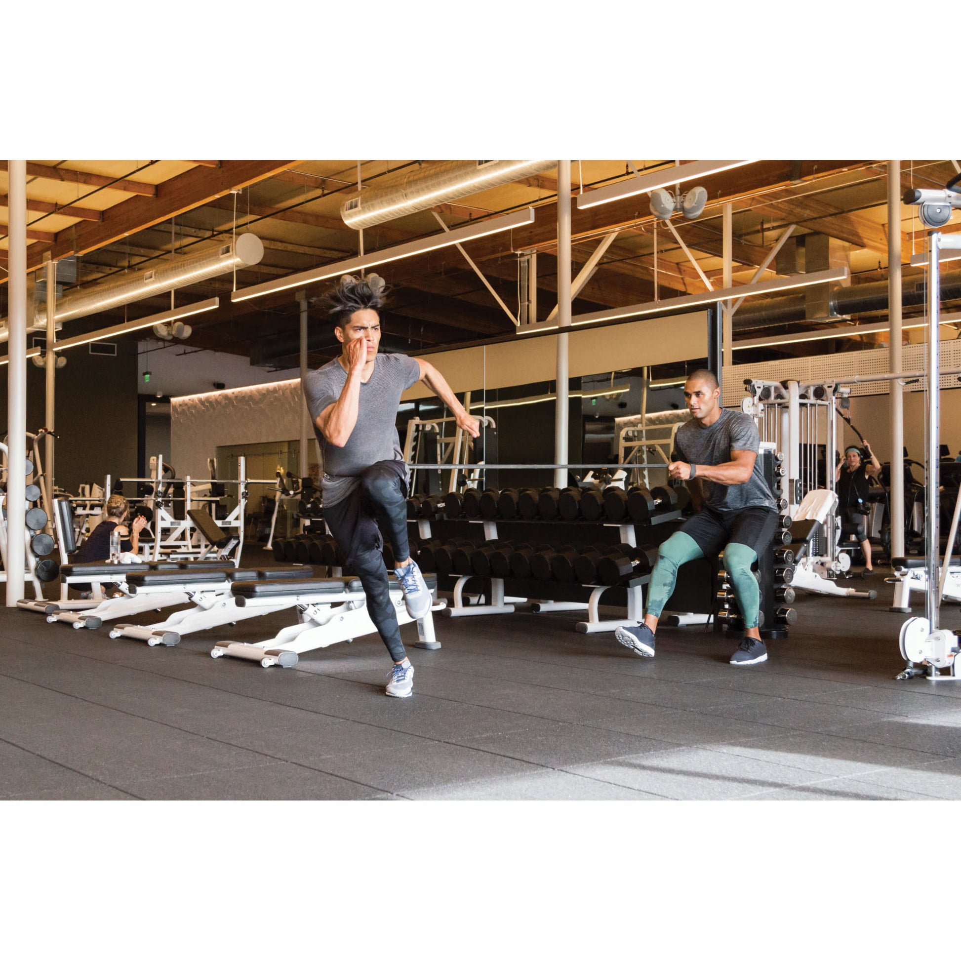 Person runs on a treadmill while trainer observes in a gym environment