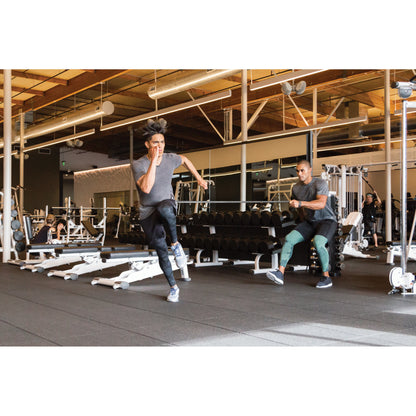 Person runs on a treadmill while trainer observes in a gym environment