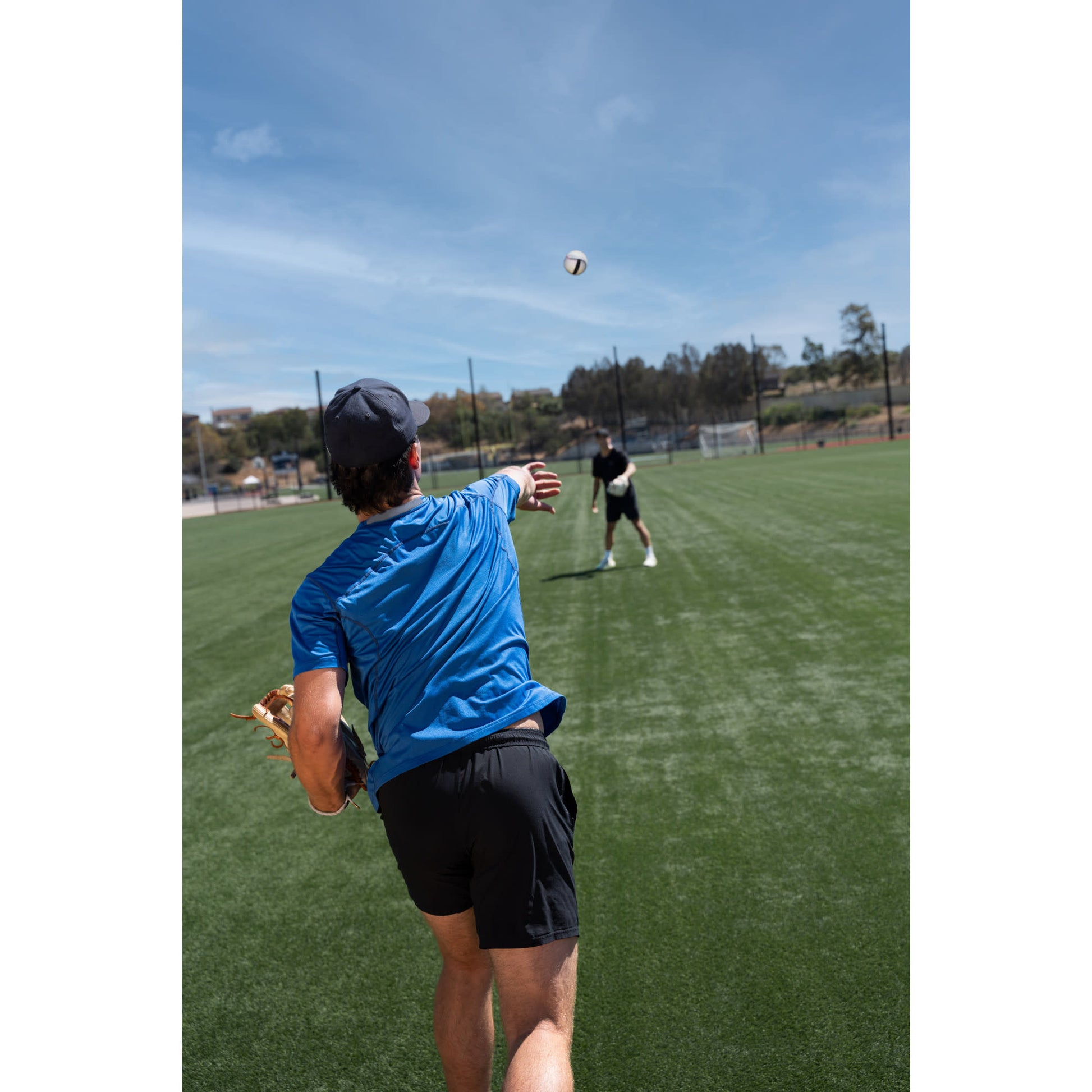 Boy throws a volleyball on a green field during outdoor practice with a coach observing.