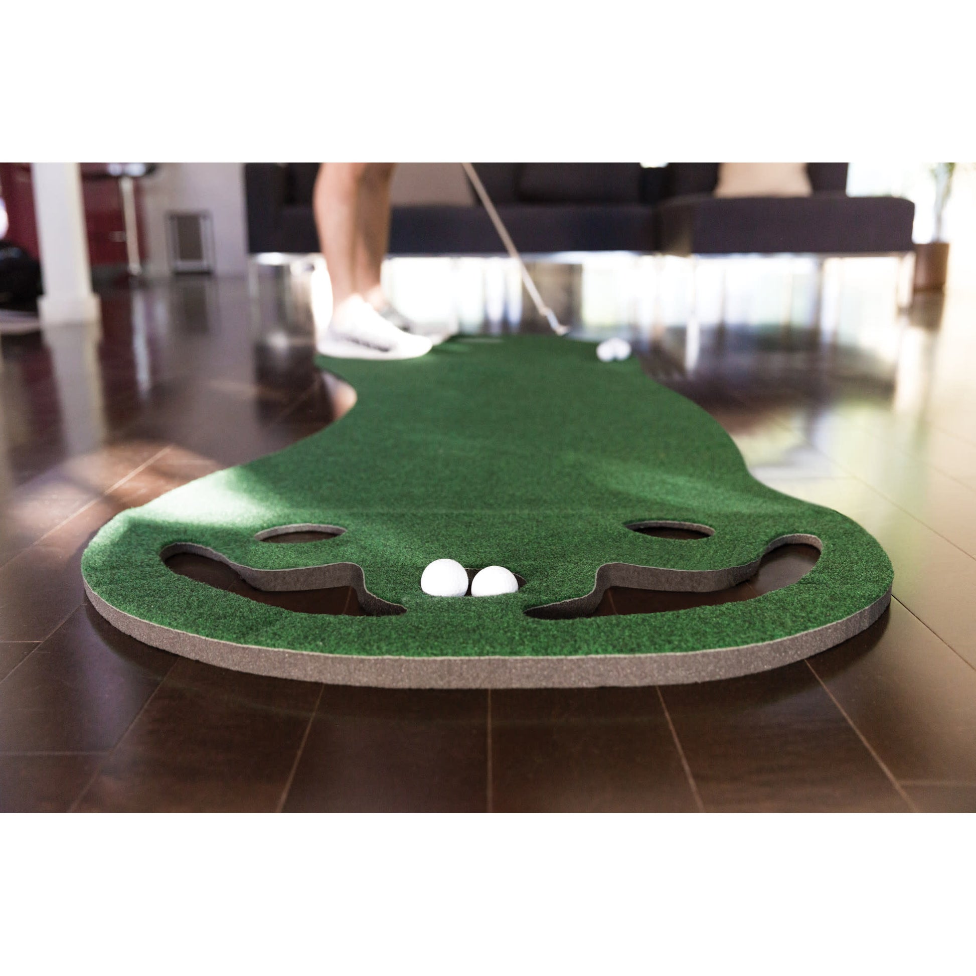 Person uses putter to hit golf balls on indoor mini golf course with artificial grass surface