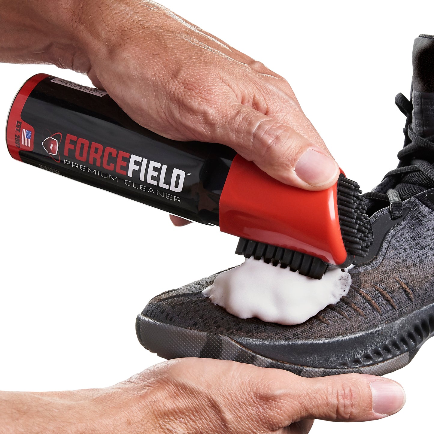 A hand applies cleaning foam to a shoe using a spray bottle labeled Forge Field.