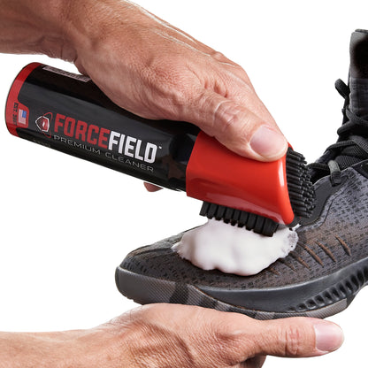 A hand applies cleaning foam to a shoe using a spray bottle labeled Forge Field.