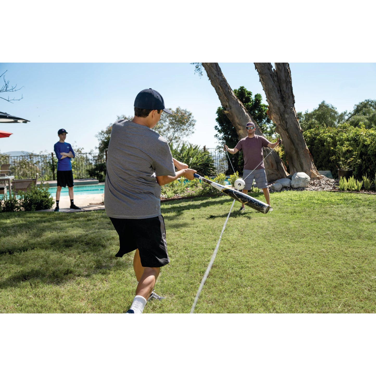 Boy pulls on a rope connected to a drone in a backyard with two men watching