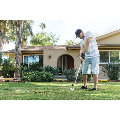 Man practices golf on lawn outside house with trees and bushes in the background