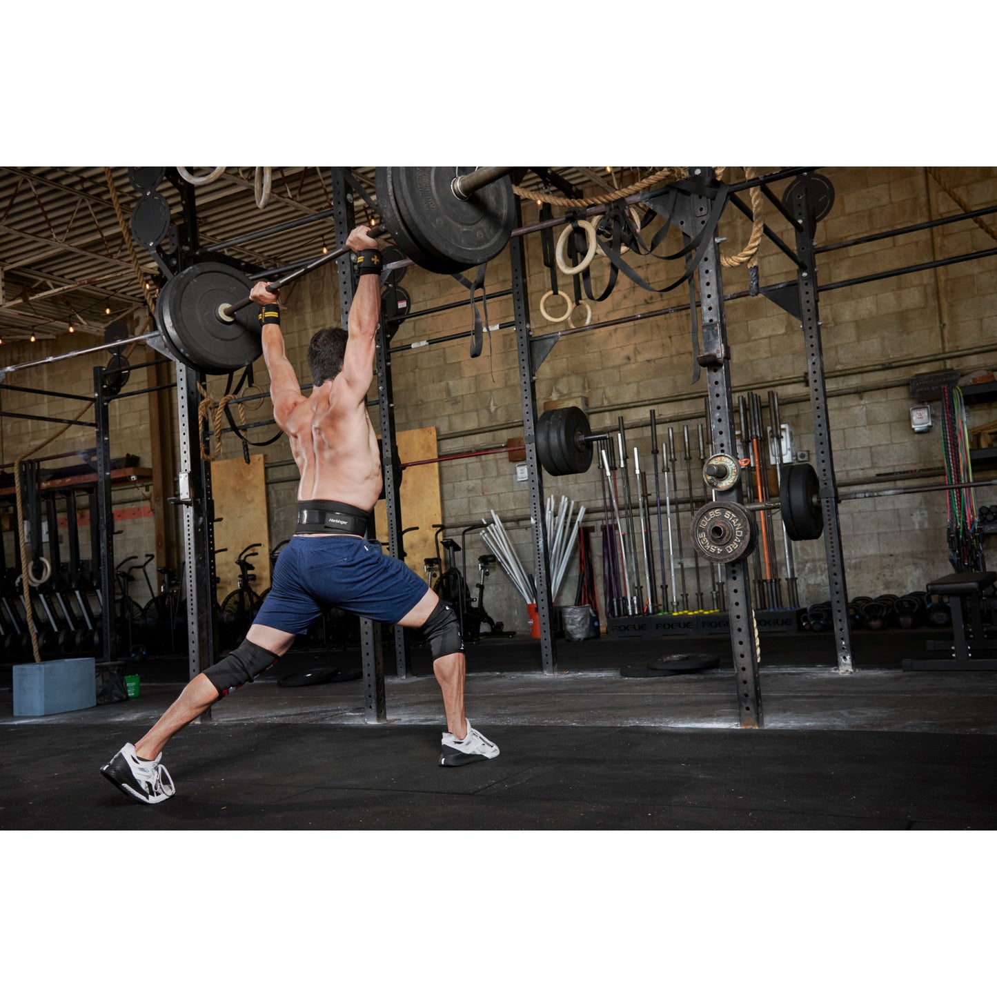 Man lifts barbell overhead in gym surrounded by weightlifting equipment.