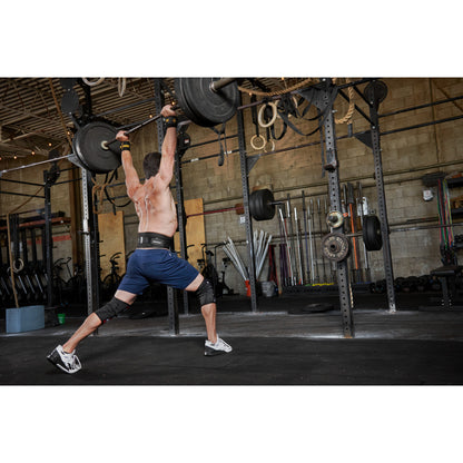 Man lifts barbell overhead in gym surrounded by weightlifting equipment.