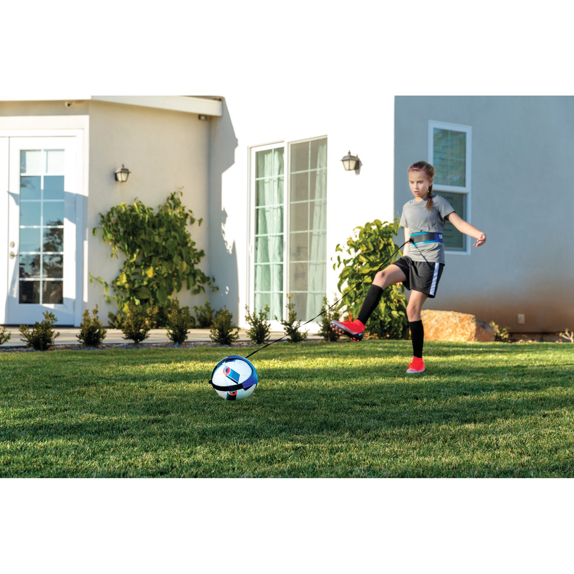 Girl kicks soccer ball on grassy lawn in front of modern house