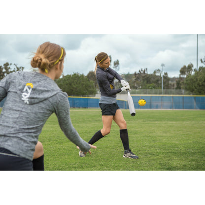 Player swings a bat at a yellow ball during outdoor practice on a grassy field