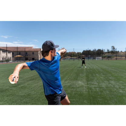 A boy throws a baseball on a grassy field under a clear blue sky.