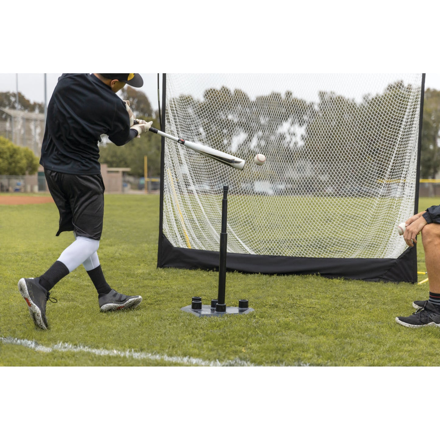Action shot of male using SKLZ 5-position tee on a field hitting into a net