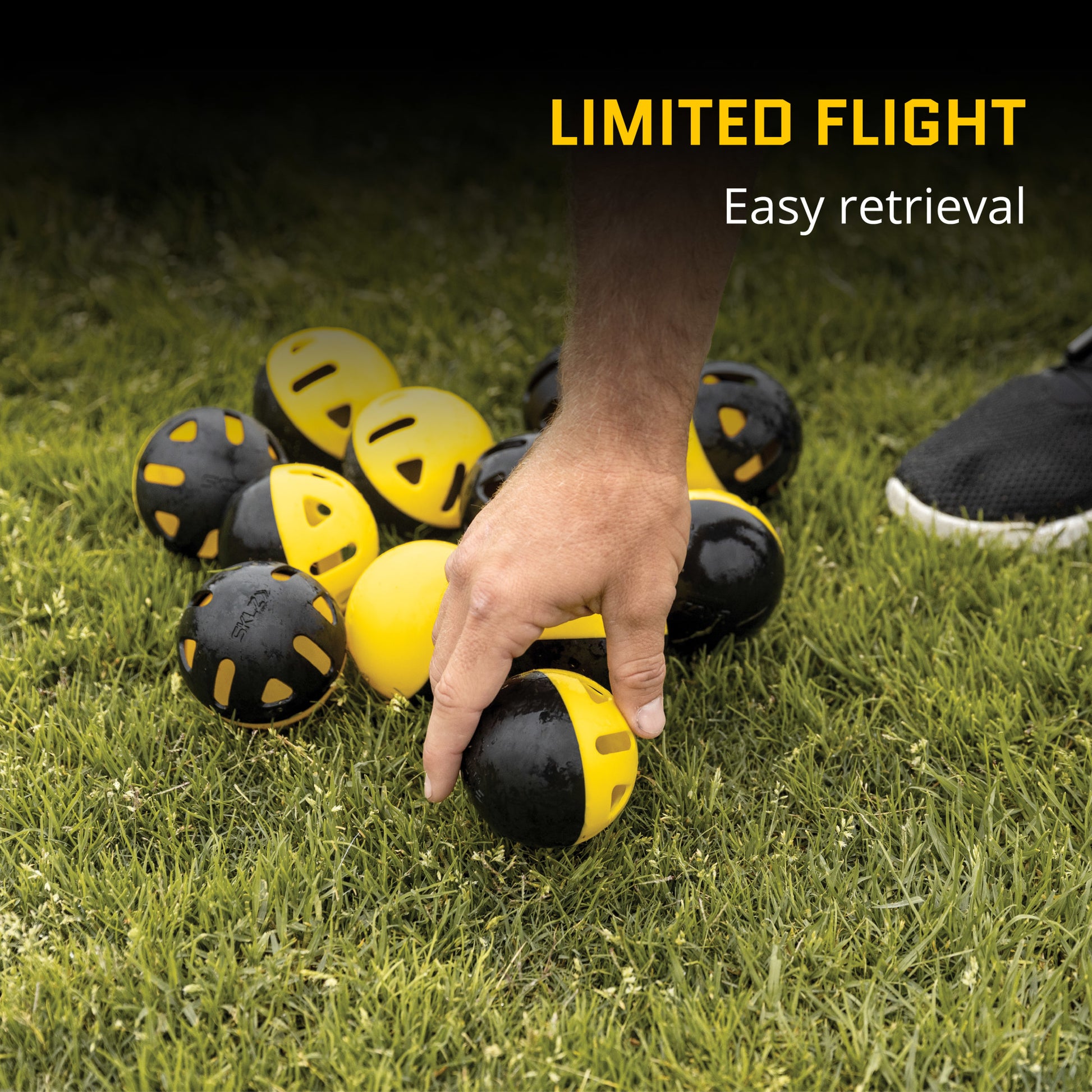 A hand picks up a yellow and black ball on grass for limited flight practice