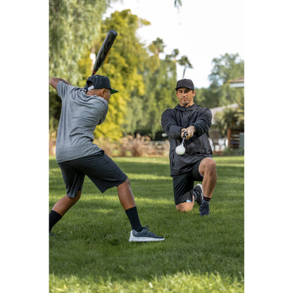 Two boys practice baseball outdoors on a grassy field with trees in the background