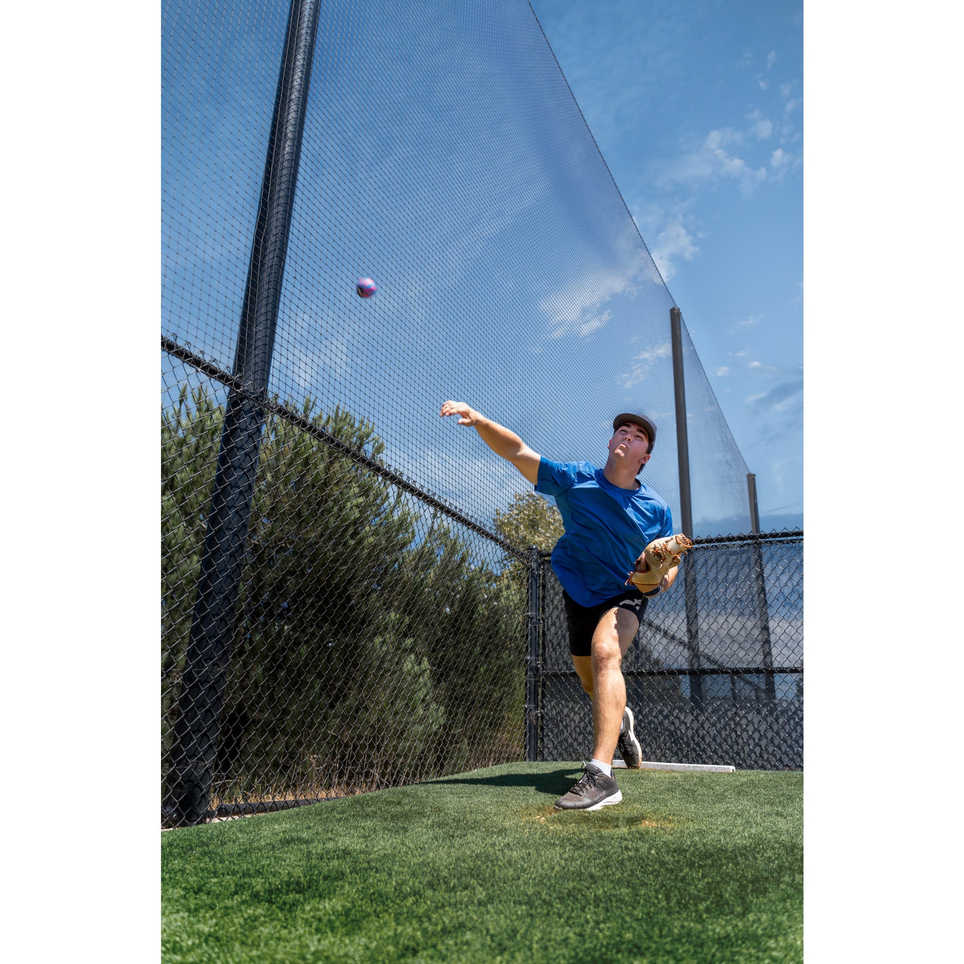 Player throws ball on outdoor baseball field with fence and blue sky background