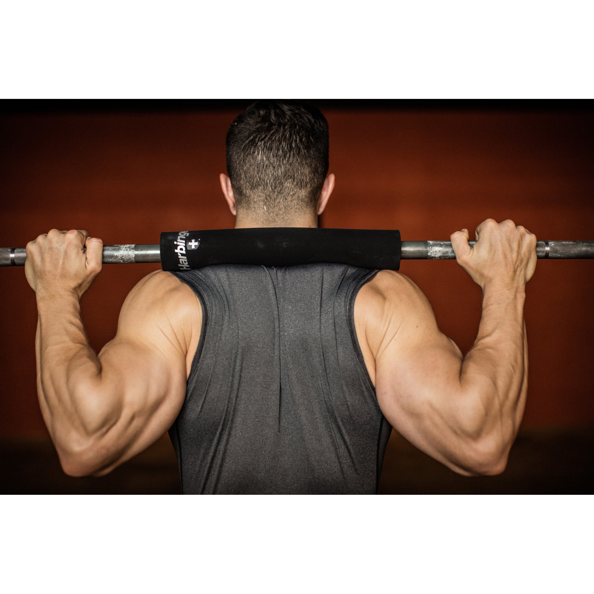 Man lifting barbell on shoulders in gym setting.