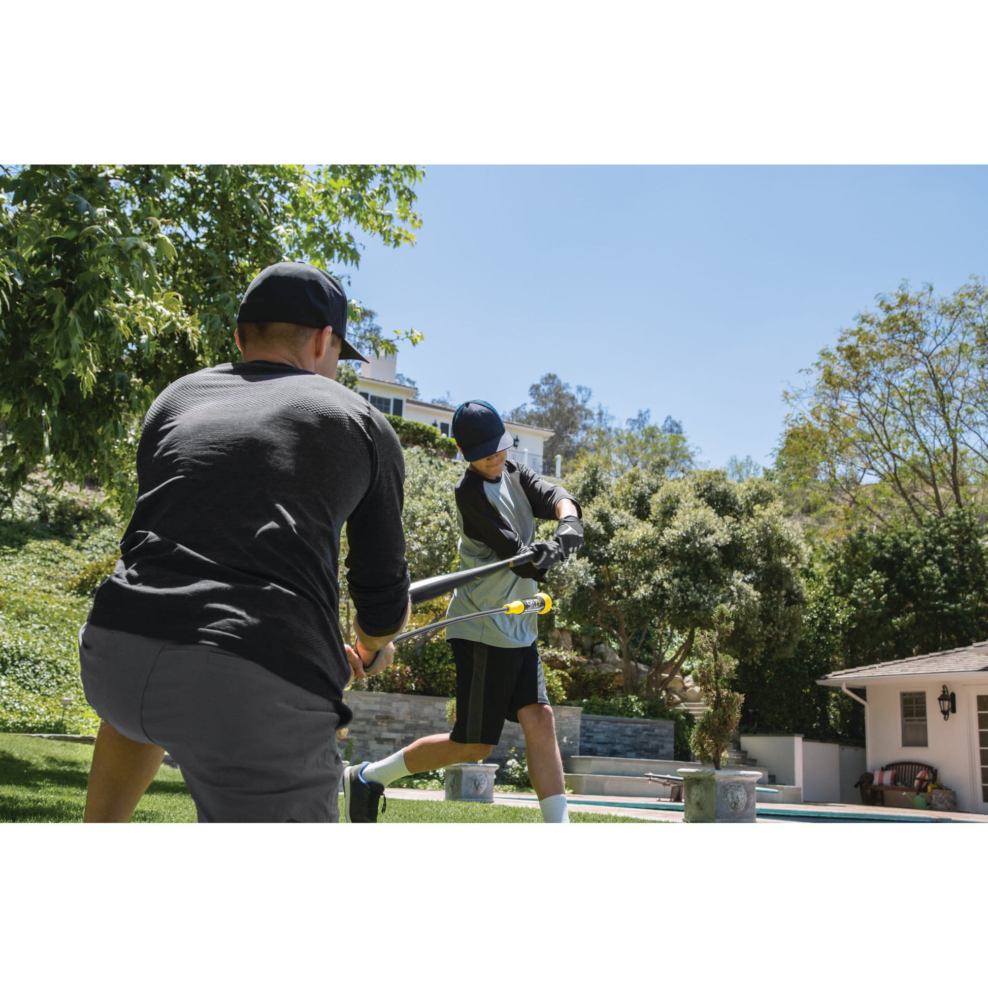 Two people trim bushes using hedge shears in a backyard garden on a sunny day