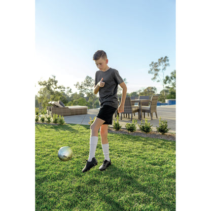 Boy practices golf with a club and ball on the lawn in a backyard patio area