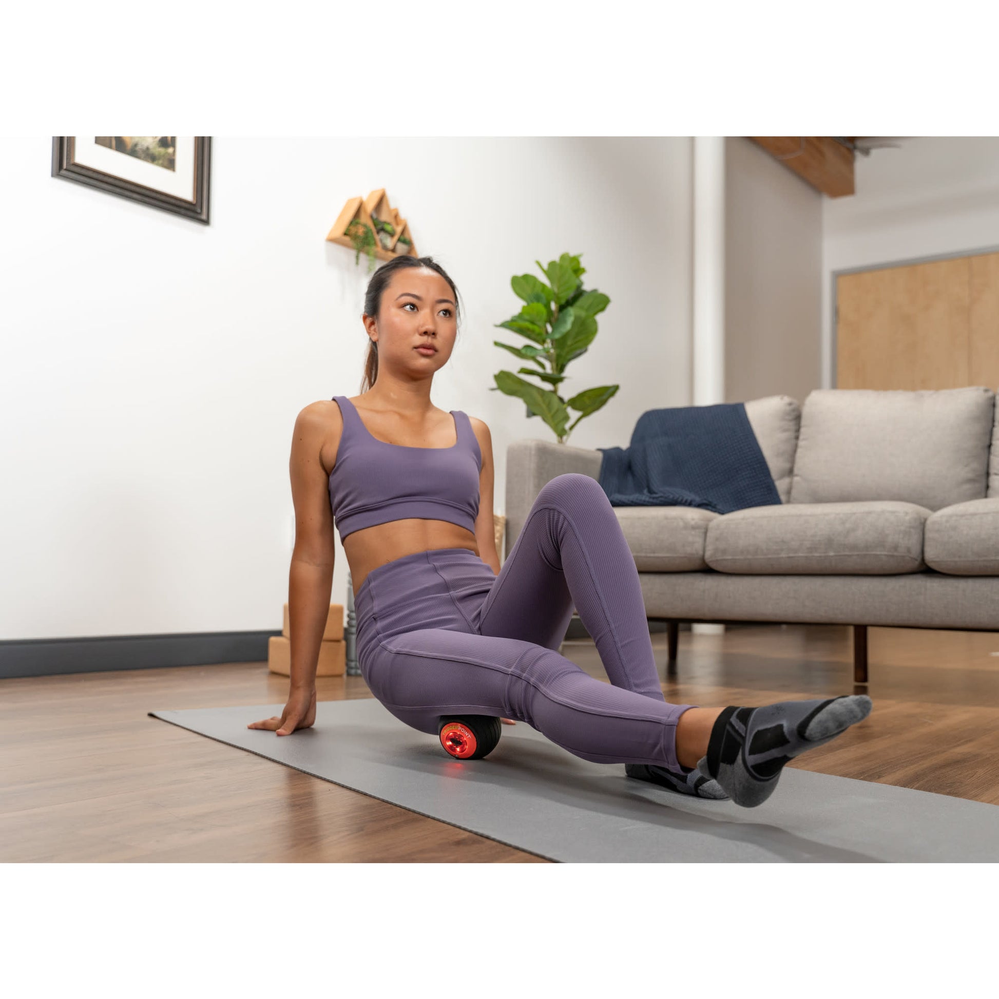 Woman exercises with a foam roller on a yoga mat in a living room.