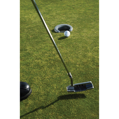 A golf putter strikes the ball on the green near a hole with a golf ball and cup nearby