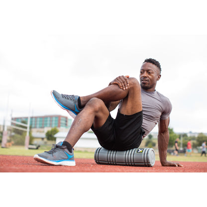 Man performs stretching exercise on a foam roller outdoors at a sports field.