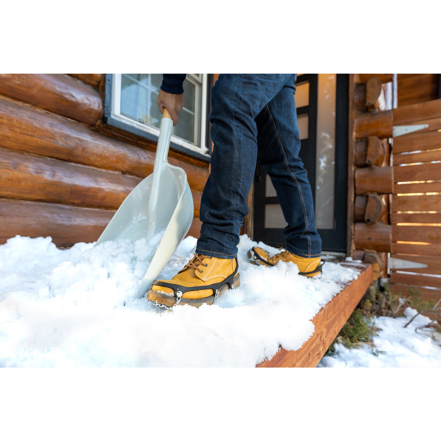 Person shoveling snow outside a cabin wearing yellow boots and jeans