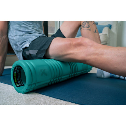 Person stretches leg on foam roller during workout on blue mat at home.