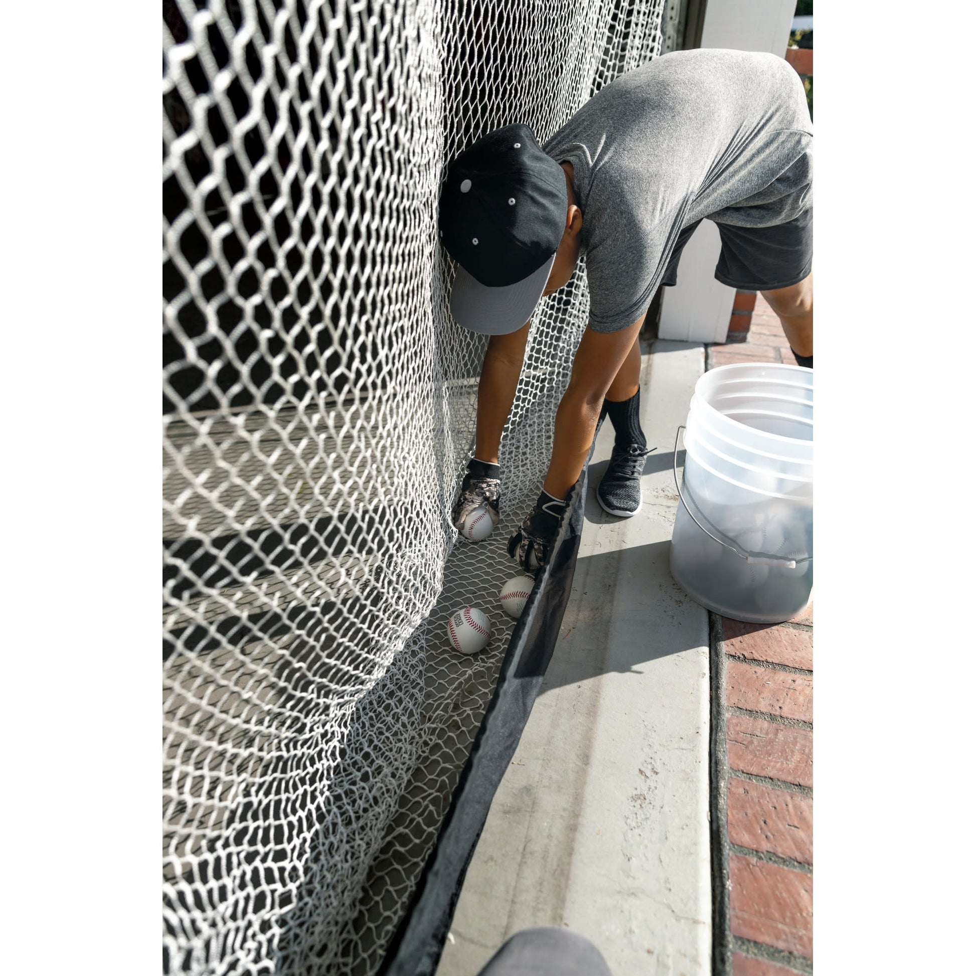 Person prepares baseballs against a fence outdoors for practice or training